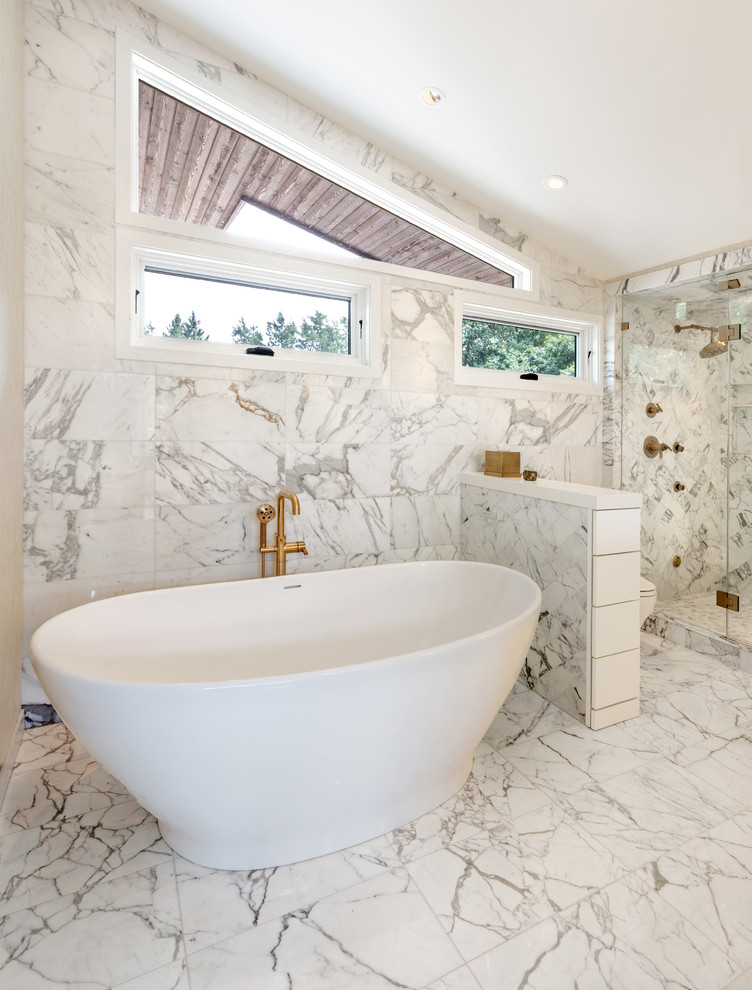 Photo of a contemporary 3/4 bathroom in Milwaukee with white cabinets, a freestanding tub, white tile, marble, white walls, marble floors, white floor, a hinged shower door, flat-panel cabinets, a one-piece toilet, a drop-in sink, engineered quartz benchtops and white benchtops.