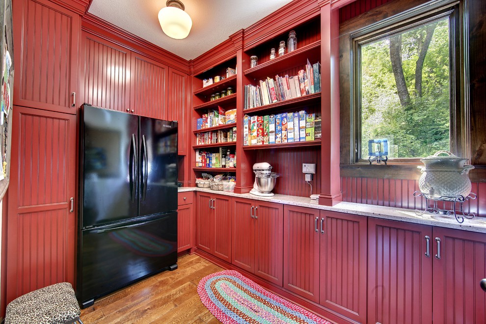 Country kitchen pantry in Minneapolis with beaded inset cabinets, red cabinets, granite benchtops, red splashback, timber splashback, black appliances, medium hardwood floors and brown floor.
