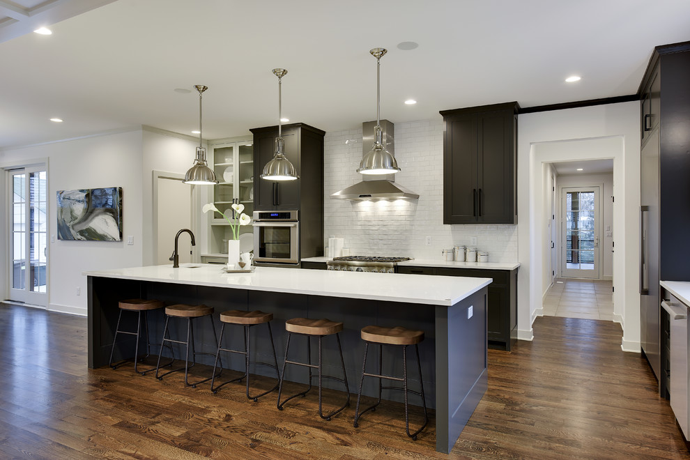 Large transitional l-shaped eat-in kitchen in Minneapolis with an undermount sink, shaker cabinets, grey cabinets, white splashback, stainless steel appliances, dark hardwood floors, with island and brown floor.