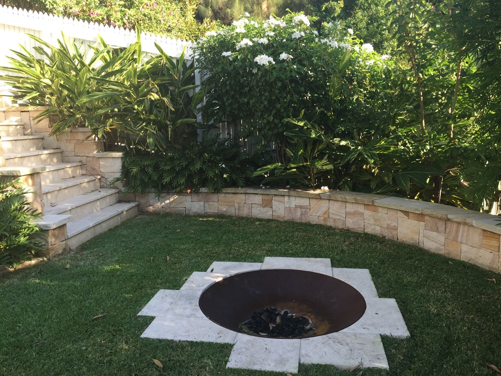 Inspiration for a mid-sized tropical backyard partial sun formal garden in Brisbane with natural stone pavers and a fire feature.