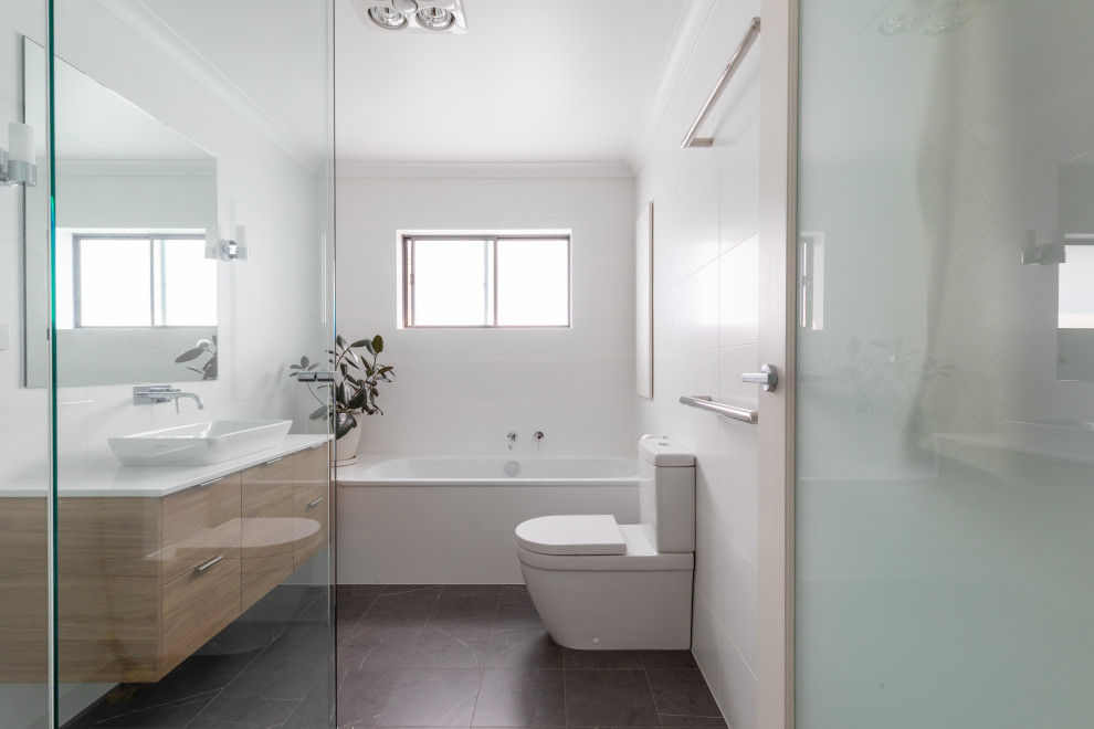 Inspiration for a mid-sized contemporary master bathroom in Canberra - Queanbeyan with flat-panel cabinets, light wood cabinets, a drop-in tub, a corner shower, a two-piece toilet, white tile, porcelain tile, white walls, porcelain floors, a trough sink, engineered quartz benchtops, grey floor, a hinged shower door and white benchtops.