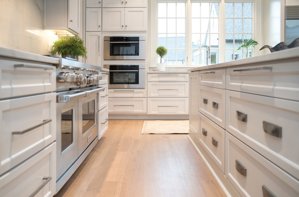 Design ideas for a mid-sized transitional l-shaped eat-in kitchen in Other with an undermount sink, shaker cabinets, white cabinets, quartzite benchtops, white splashback, stone tile splashback, light hardwood floors, with island and white benchtop.