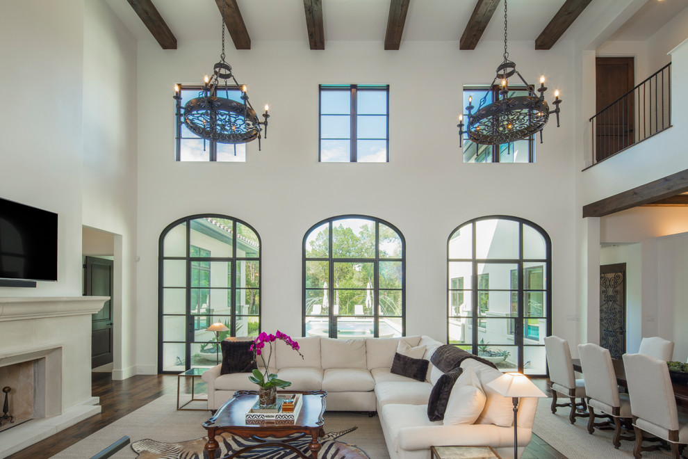 This is an example of a large mediterranean formal open concept living room in Austin with beige walls, dark hardwood floors, a standard fireplace, a stone fireplace surround and brown floor.