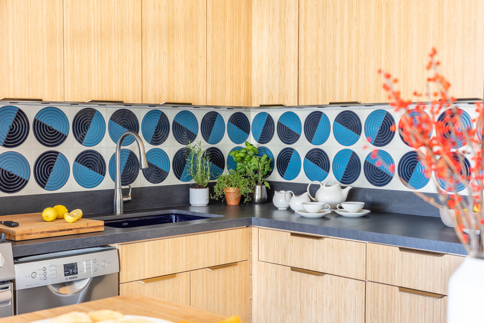 Design ideas for a small eclectic l-shaped open plan kitchen in Chicago with an undermount sink, flat-panel cabinets, light wood cabinets, solid surface benchtops, blue splashback, ceramic splashback, stainless steel appliances, ceramic floors, with island, blue floor and black benchtop.