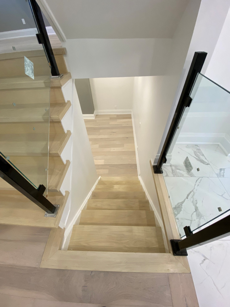 This is an example of a medium sized modern wood l-shaped glass railing staircase in Toronto with wood risers and panelled walls.