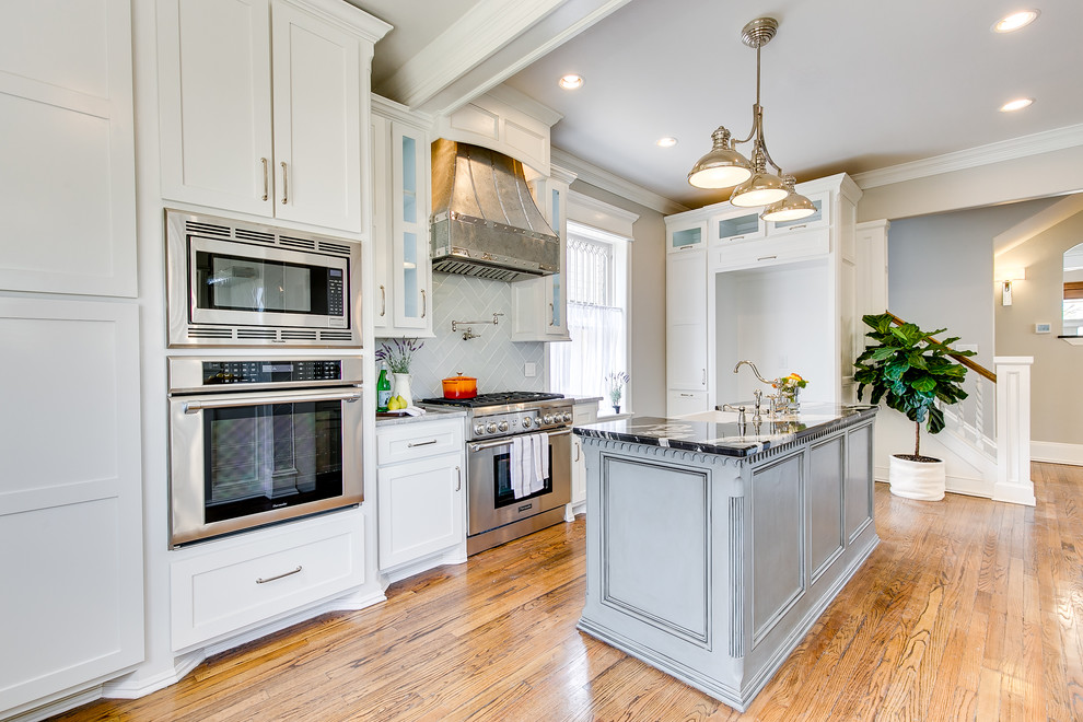 This is an example of a large transitional galley separate kitchen in Oklahoma City with a farmhouse sink, recessed-panel cabinets, white cabinets, granite benchtops, grey splashback, glass tile splashback, stainless steel appliances, medium hardwood floors, with island, brown floor and grey benchtop.