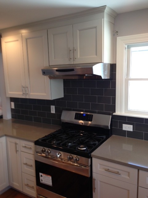 Example of a small transitional l-shaped medium tone wood floor kitchen design in Boston with shaker cabinets, white cabinets, quartzite countertops, gray backsplash, ceramic backsplash and stainless steel appliances