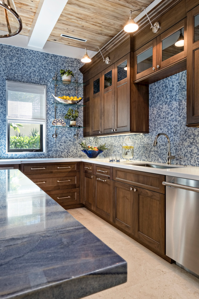 This is an example of a large transitional l-shaped kitchen in Other with an undermount sink, shaker cabinets, medium wood cabinets, blue splashback, stainless steel appliances, with island, beige floor and white benchtop.