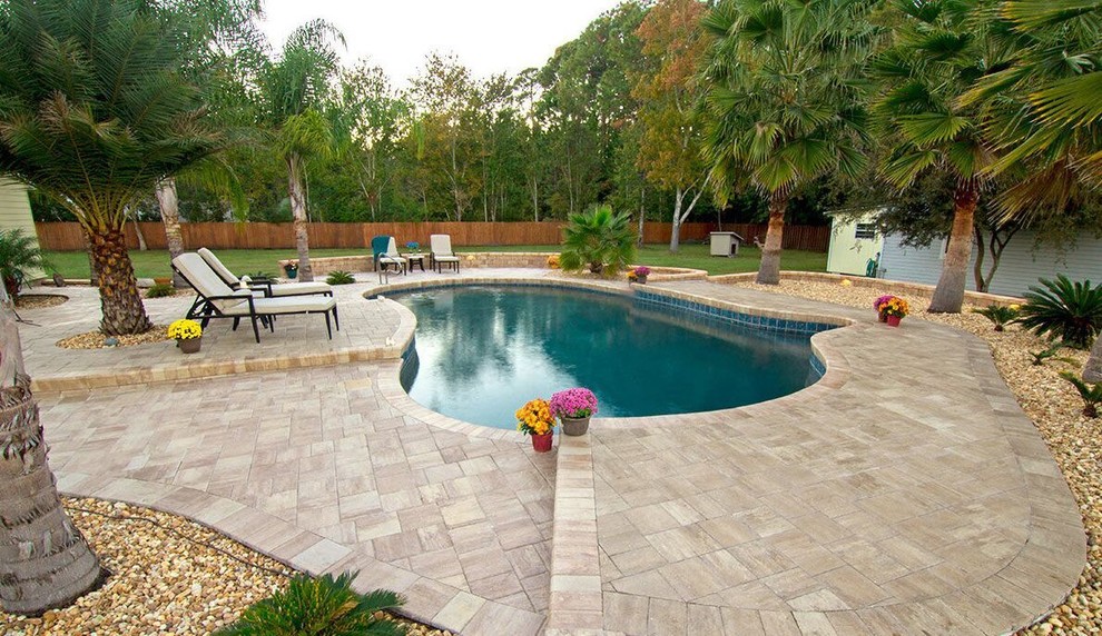 This is an example of a mid-sized traditional backyard custom-shaped infinity pool in Tampa with natural stone pavers.