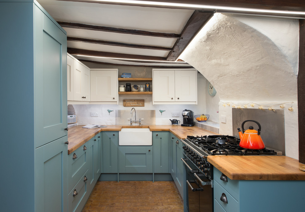 Mid-sized country u-shaped separate kitchen in Kent with a farmhouse sink, shaker cabinets, blue cabinets, wood benchtops, vinyl floors, panelled appliances, no island and brown floor.