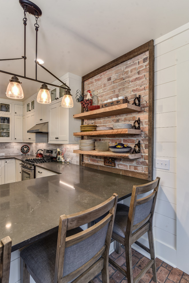Inspiration for a country u-shaped kitchen in Other with a farmhouse sink, shaker cabinets, white cabinets, beige splashback, brick splashback, stainless steel appliances, brick floors, a peninsula and quartz benchtops.