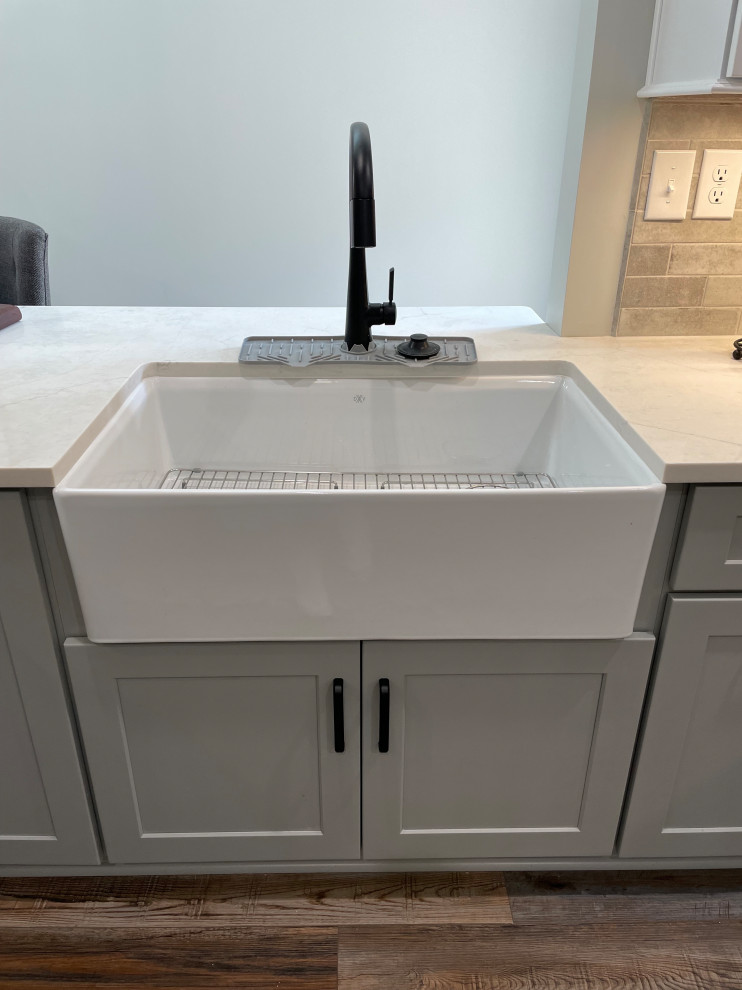 Inspiration for a mid-sized transitional vinyl floor and brown floor eat-in kitchen remodel with a farmhouse sink, shaker cabinets, white cabinets, quartz countertops, gray backsplash, subway tile backsplash, no island and white countertops