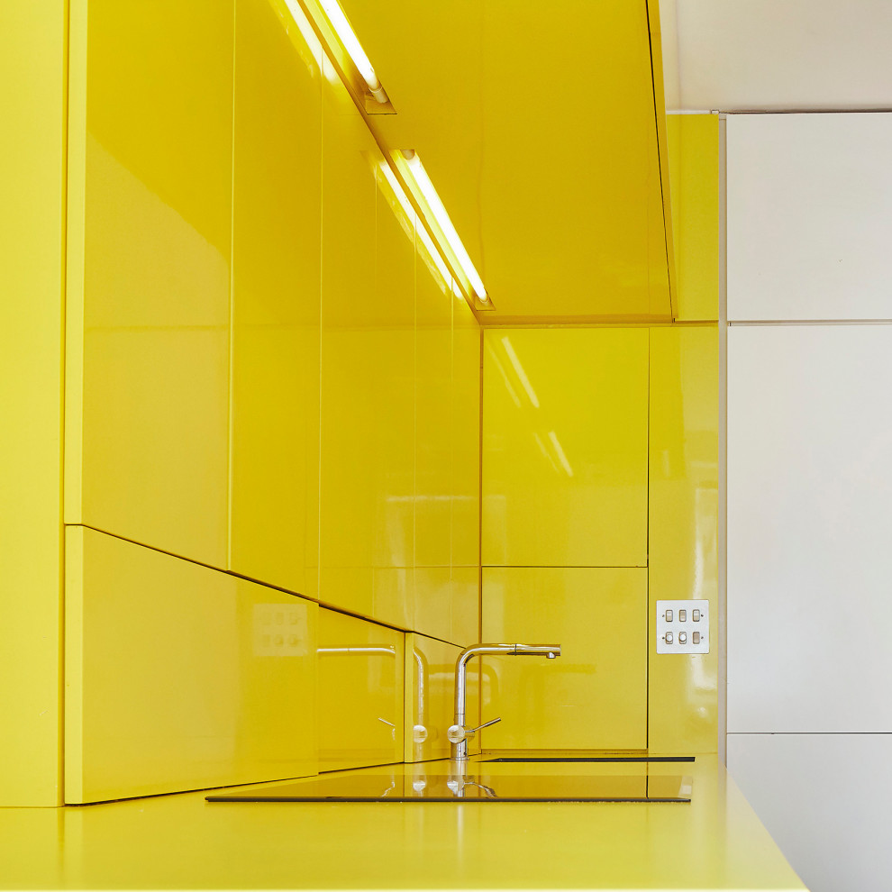 Small contemporary single-wall open plan kitchen in London with a built-in sink, flat-panel cabinets, yellow cabinets, laminate countertops, yellow splashback, light hardwood flooring, no island and yellow worktops.