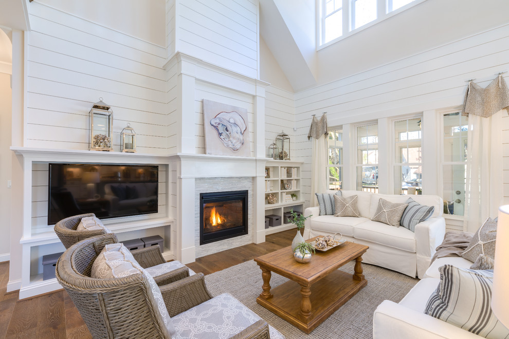 Inspiration for a beach style enclosed family room in Other with white walls, medium hardwood floors, a standard fireplace, a stone fireplace surround, a wall-mounted tv and brown floor.
