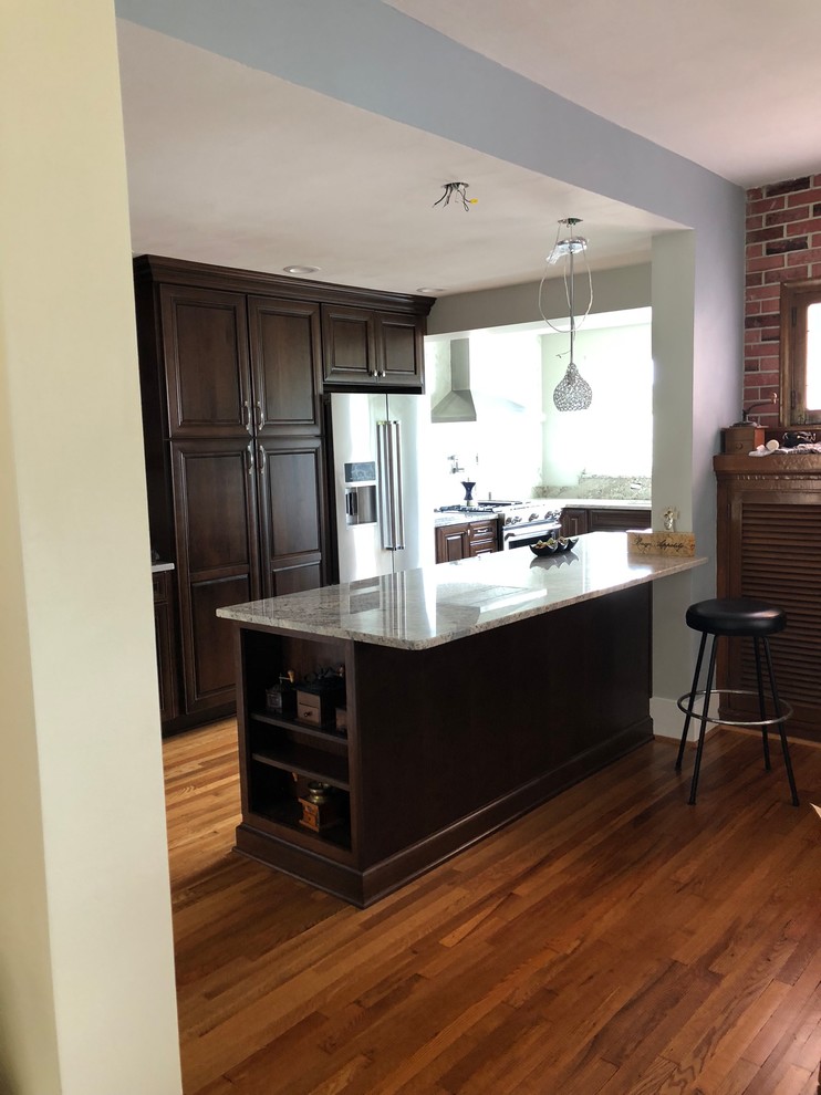 Mid-sized elegant l-shaped light wood floor and brown floor eat-in kitchen photo with an undermount sink, raised-panel cabinets, dark wood cabinets, granite countertops, multicolored backsplash, ceramic backsplash, stainless steel appliances, an island and multicolored countertops