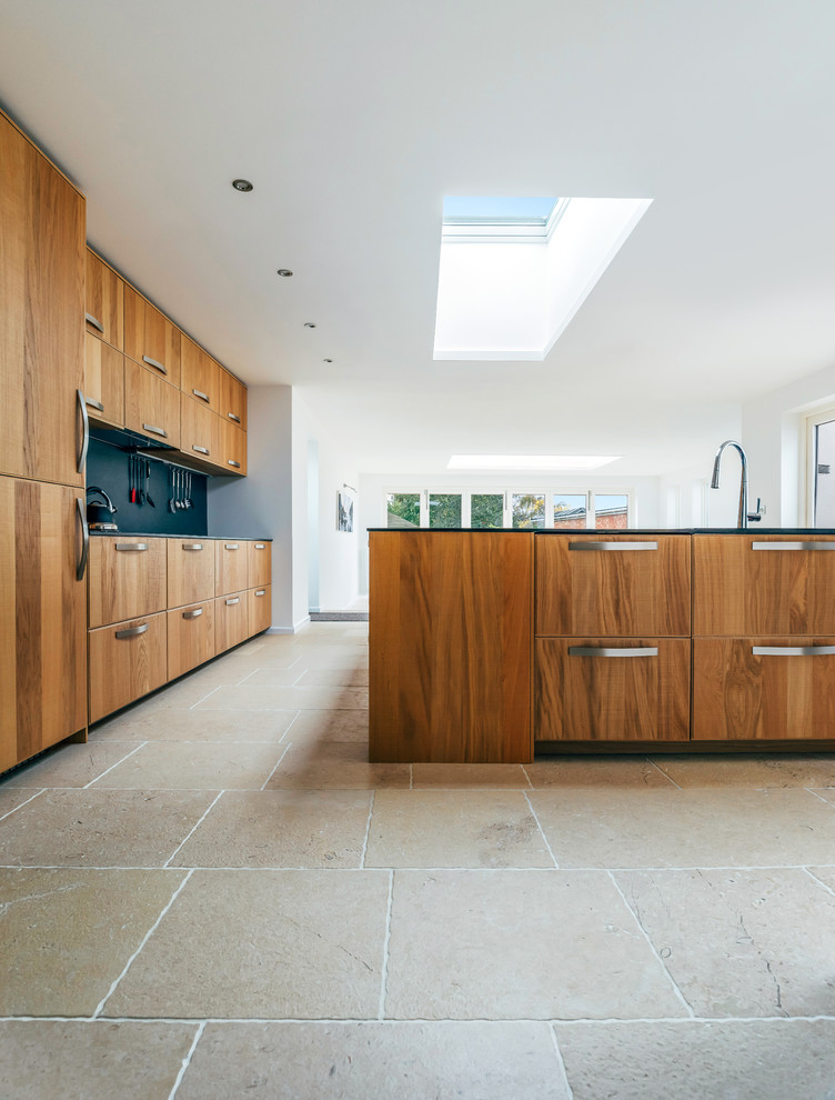 Design ideas for a large contemporary galley kitchen in Cambridgeshire with flat-panel cabinets, dark wood cabinets, solid surface benchtops, black splashback, stainless steel appliances, limestone floors, with island, beige floor and black benchtop.