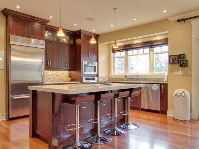 This is an example of a mid-sized traditional l-shaped eat-in kitchen in Calgary with an undermount sink, shaker cabinets, medium wood cabinets, quartz benchtops, multi-coloured splashback, mosaic tile splashback, stainless steel appliances, medium hardwood floors and with island.