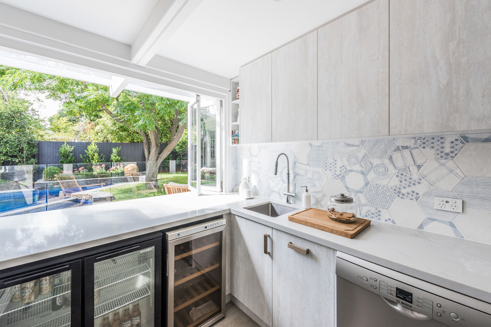 Mid-sized contemporary u-shaped kitchen in Melbourne with an undermount sink, flat-panel cabinets, light wood cabinets, quartz benchtops, blue splashback, mosaic tile splashback, stainless steel appliances, porcelain floors, brown floor and white benchtop.