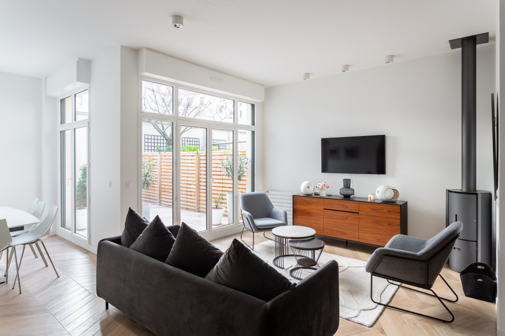 Diseño de salón actual con paredes blancas, suelo de madera clara, televisor colgado en la pared y suelo beige