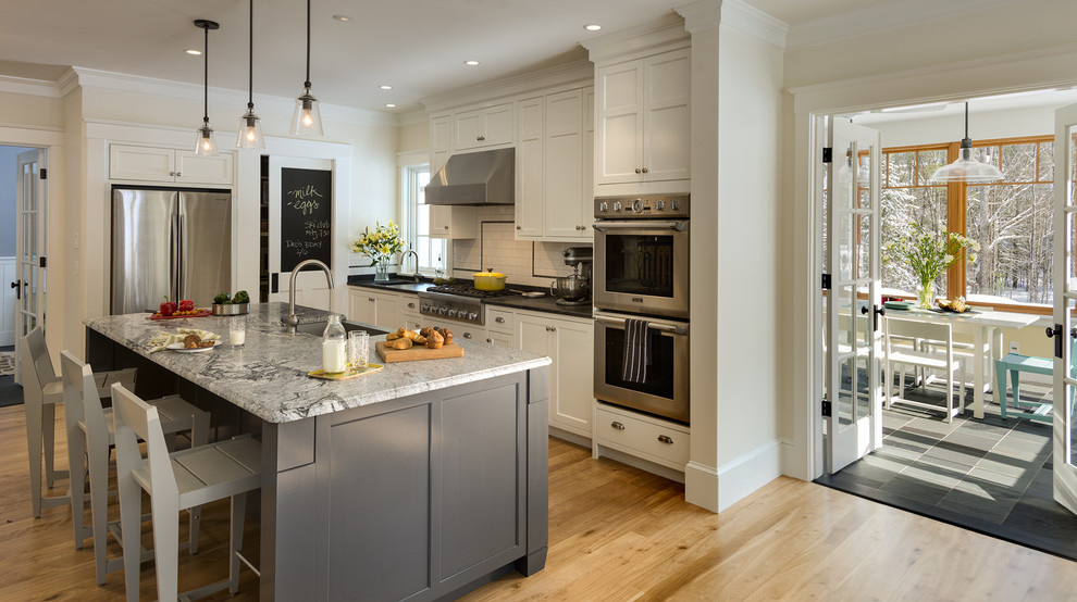 Eat-in kitchen - large traditional galley light wood floor eat-in kitchen idea in Portland Maine with a farmhouse sink, shaker cabinets, white cabinets, granite countertops, white backsplash, ceramic backsplash, stainless steel appliances and white walls