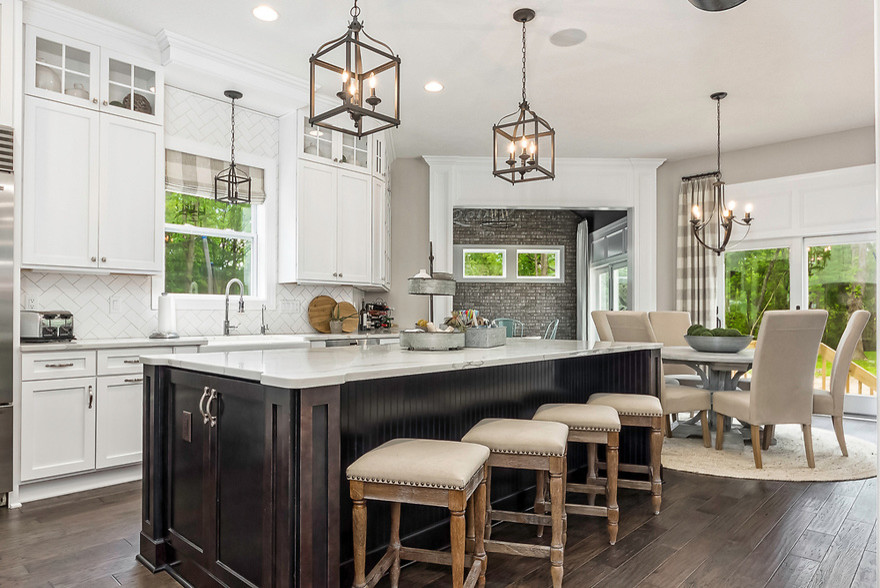 Mid-sized transitional l-shaped dark wood floor and brown floor open concept kitchen photo in Columbus with a farmhouse sink, shaker cabinets, white cabinets, marble countertops, white backsplash, porcelain backsplash, stainless steel appliances and an island