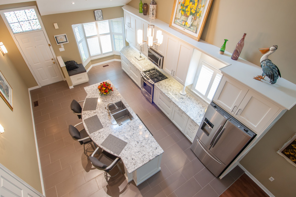 Inspiration for a mid-sized transitional galley ceramic tile eat-in kitchen remodel in Toronto with a double-bowl sink, shaker cabinets, white cabinets, granite countertops, beige backsplash, stone tile backsplash, stainless steel appliances and an island