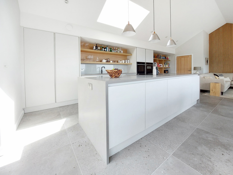 Design ideas for a large scandinavian single-wall open plan kitchen in Cornwall with an integrated sink, flat-panel cabinets, white cabinets, quartzite benchtops, white splashback, glass sheet splashback, panelled appliances, porcelain floors, grey floor, grey benchtop and vaulted.