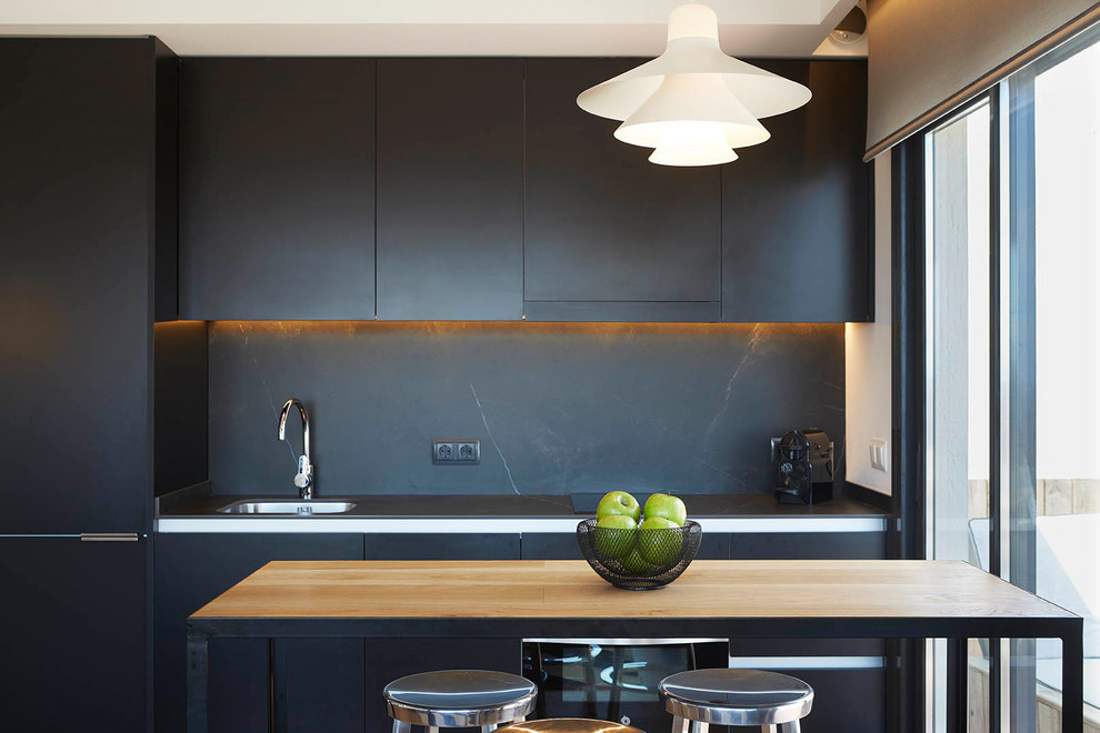 Photo of a contemporary single-wall kitchen in Barcelona with a drop-in sink, flat-panel cabinets, black cabinets, black splashback and with island.