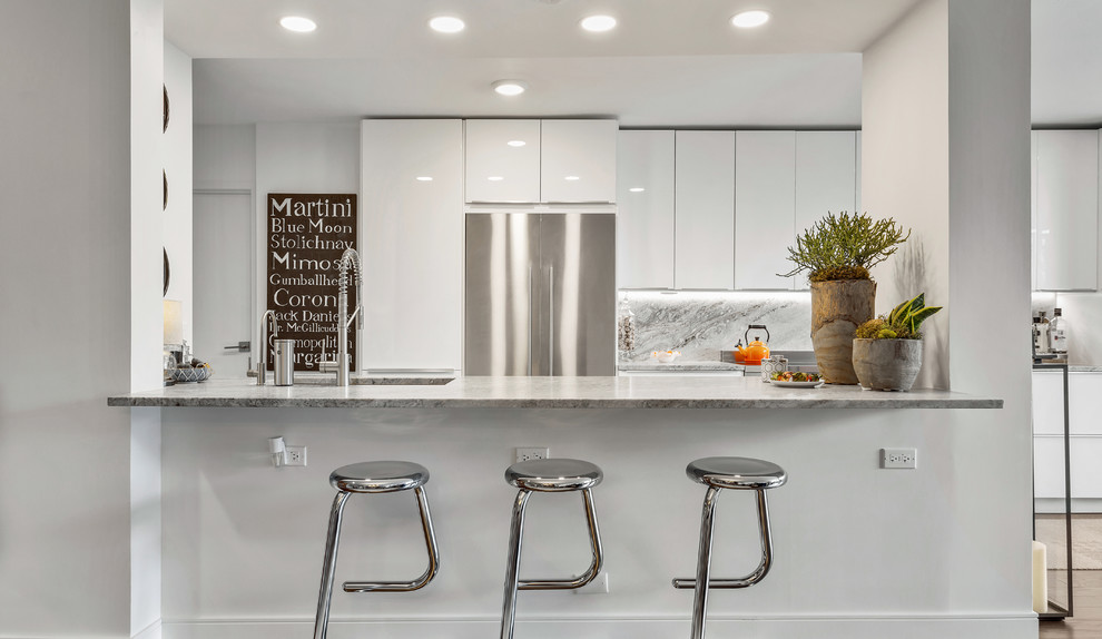 Design ideas for a mid-sized contemporary l-shaped eat-in kitchen in Chicago with an undermount sink, flat-panel cabinets, white cabinets, granite benchtops, white splashback, marble splashback, stainless steel appliances, medium hardwood floors, with island and white benchtop.