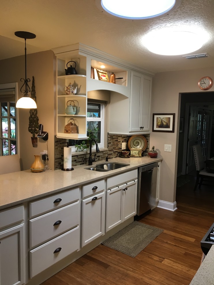 Design ideas for a mid-sized traditional galley open plan kitchen in Orlando with an undermount sink, recessed-panel cabinets, beige cabinets, quartz benchtops, metallic splashback, glass tile splashback, stainless steel appliances, laminate floors, brown floor and beige benchtop.