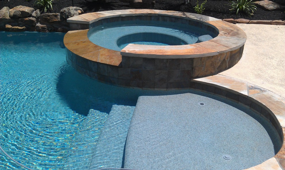 This is an example of a mid-sized contemporary backyard custom-shaped pool in Houston with a hot tub.