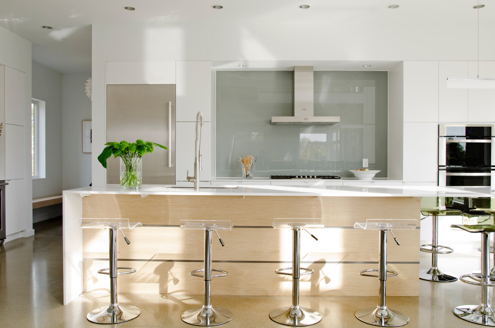 Inspiration for a contemporary kitchen in Portland Maine with an undermount sink, flat-panel cabinets, white cabinets, grey splashback, glass sheet splashback, stainless steel appliances, with island and white benchtop.