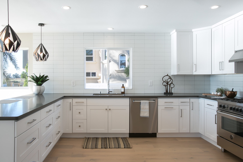 Photo of a mid-sized transitional u-shaped kitchen in San Francisco with shaker cabinets, white cabinets, quartzite benchtops, white splashback, ceramic splashback, stainless steel appliances, a peninsula, a drop-in sink, light hardwood floors and beige floor.