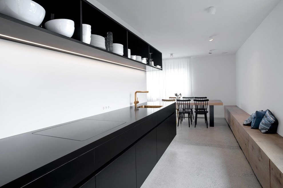 Photo of a mid-sized modern single-wall separate kitchen in Munich with a drop-in sink, flat-panel cabinets, black cabinets, white splashback, concrete floors, no island and quartz benchtops.