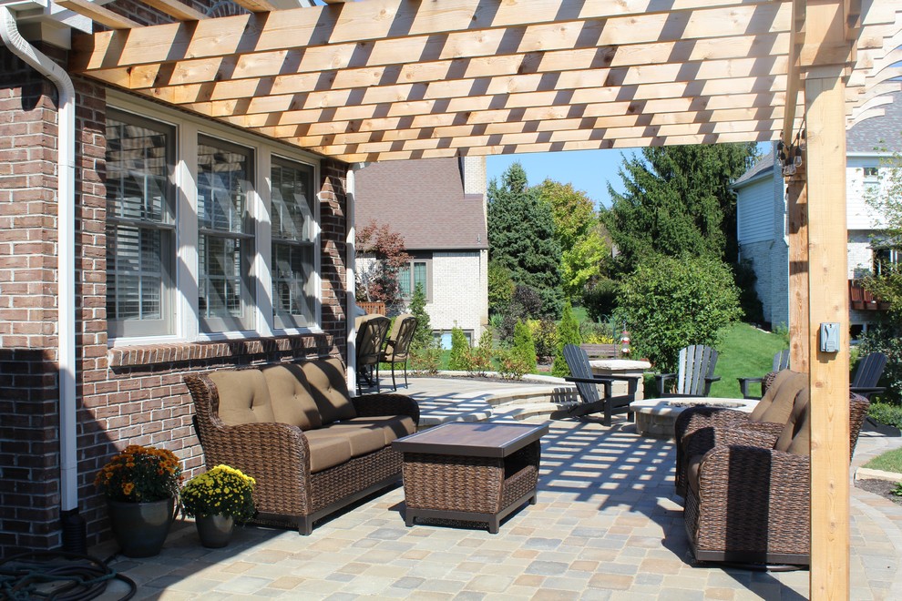 This is an example of a large traditional backyard patio in Indianapolis with a fire feature, brick pavers and a pergola.