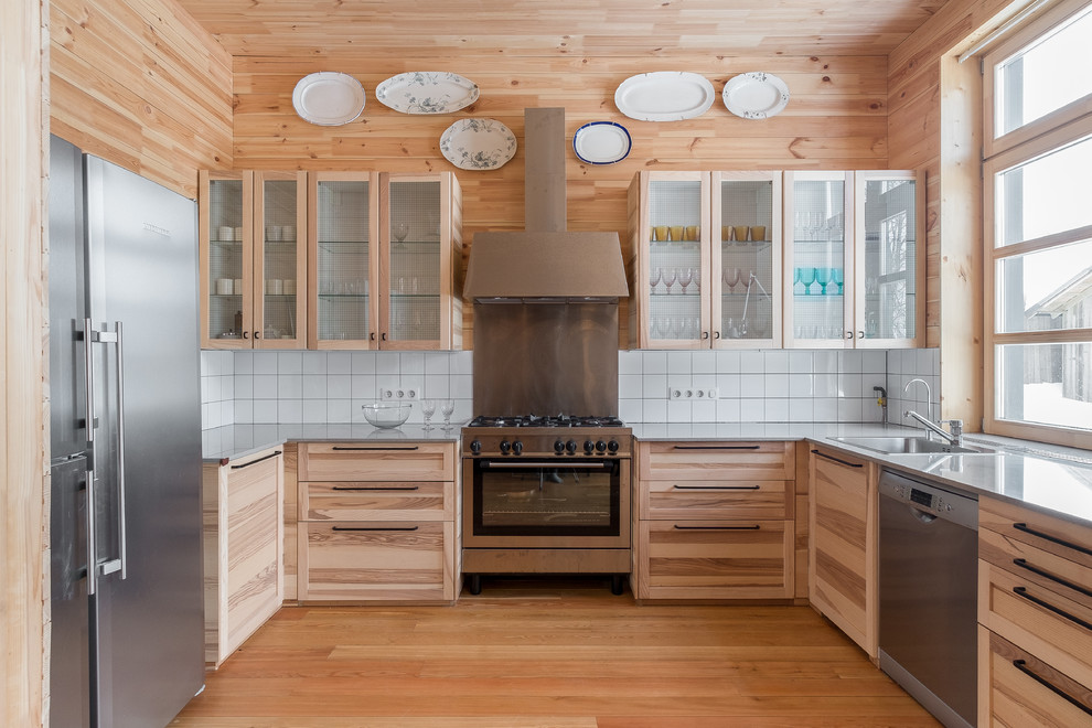 This is an example of a country u-shaped kitchen in Moscow with a drop-in sink, shaker cabinets, medium wood cabinets, white splashback, stainless steel appliances, medium hardwood floors, no island, brown floor and grey benchtop.