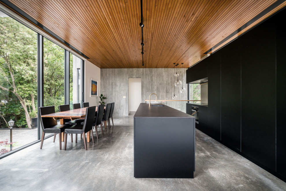 Large modern l-shaped eat-in kitchen in Christchurch with an integrated sink, flat-panel cabinets, black cabinets, metallic splashback, stainless steel appliances, with island, grey floor, black benchtop and wood.