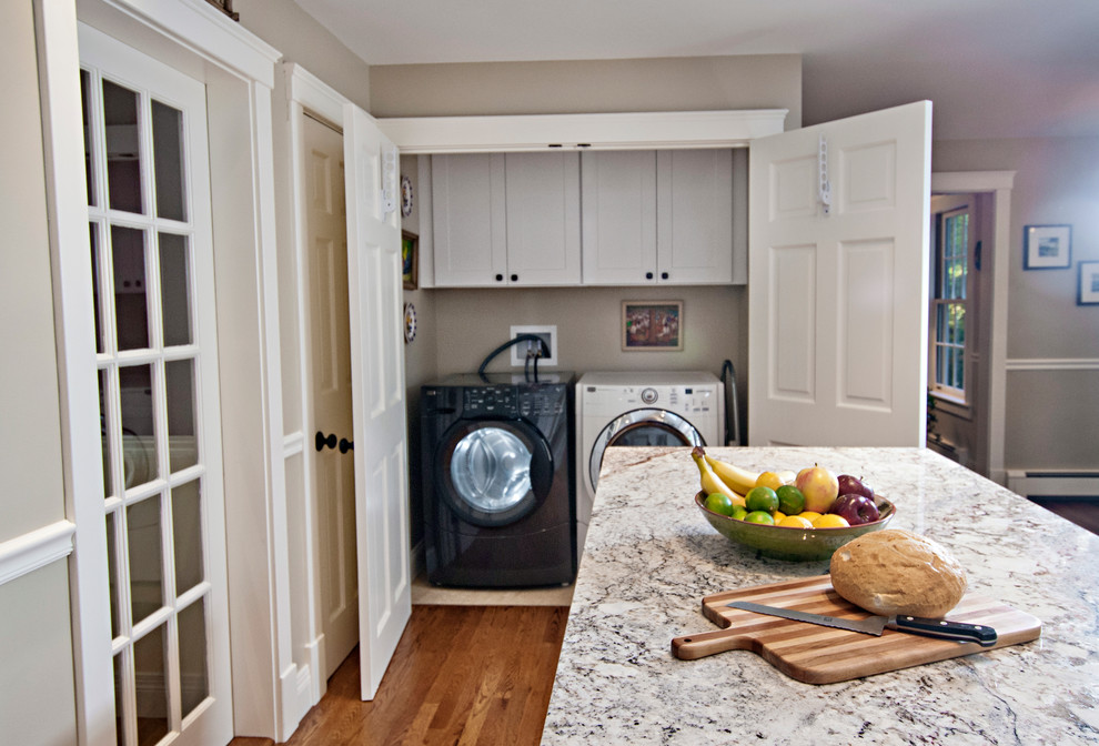 Photo of a small transitional single-wall laundry cupboard in Portland Maine with shaker cabinets, white cabinets, beige walls, linoleum floors and a side-by-side washer and dryer.