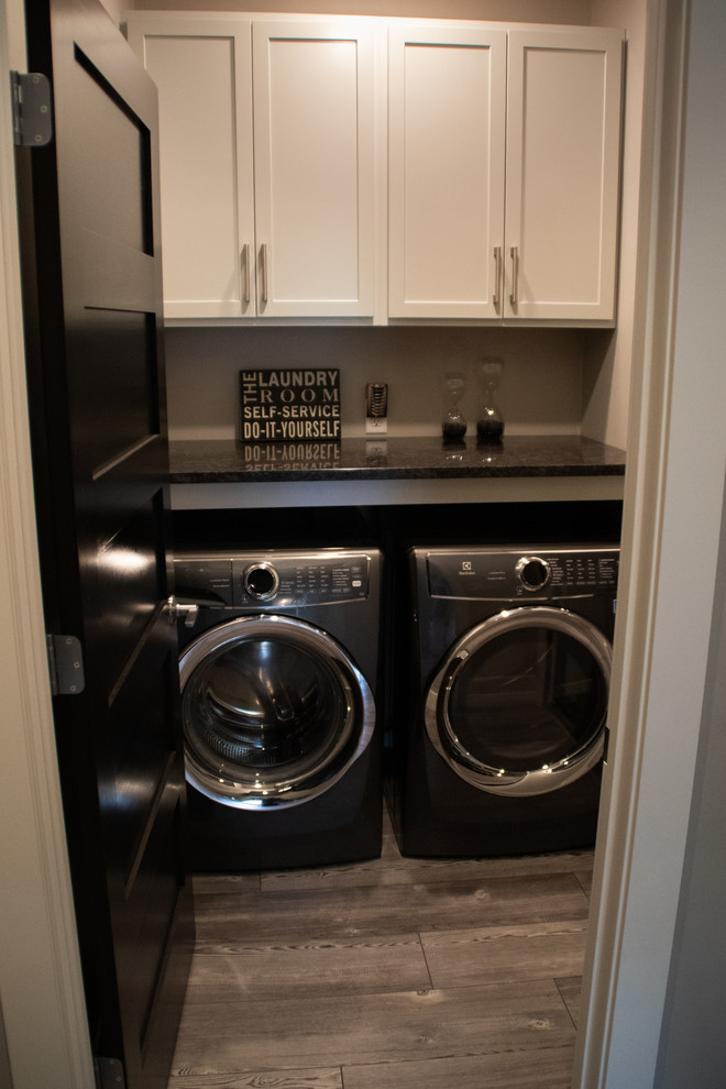Inspiration for a small industrial laundry cupboard in Other with shaker cabinets, beige cabinets, quartz benchtops, beige walls, light hardwood floors, a side-by-side washer and dryer, grey floor and black benchtop.