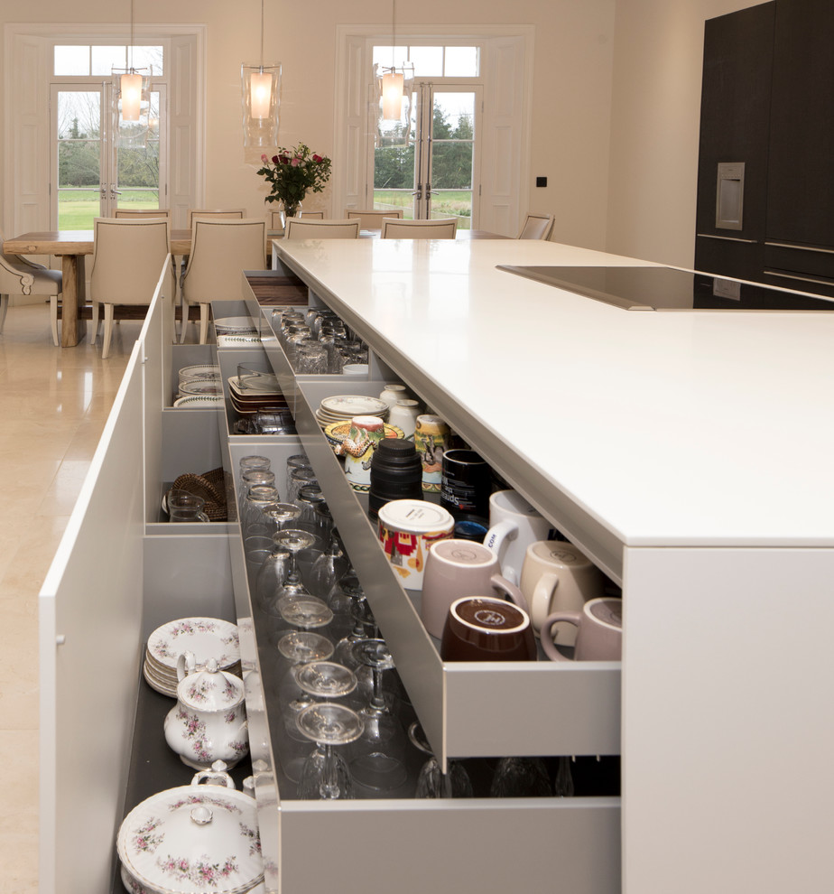 This is an example of an expansive contemporary single-wall eat-in kitchen in Wiltshire with a double-bowl sink, flat-panel cabinets, white cabinets, solid surface benchtops, white splashback, stainless steel appliances, porcelain floors and with island.