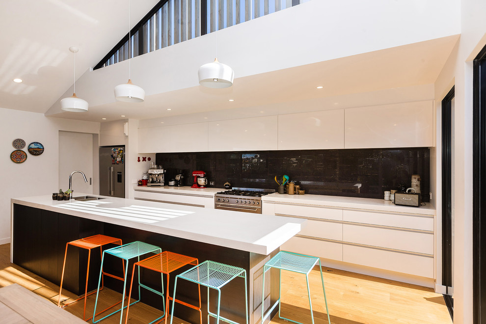 Mid-sized contemporary galley kitchen in Auckland with an undermount sink, flat-panel cabinets, white cabinets, black splashback, ceramic splashback, stainless steel appliances, medium hardwood floors, with island and orange floor.