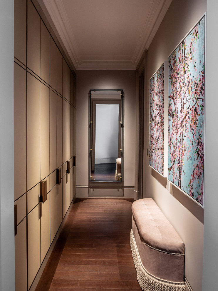 Small contemporary gender-neutral walk-in wardrobe in London with flat-panel cabinets, beige cabinets, dark hardwood floors and brown floor.