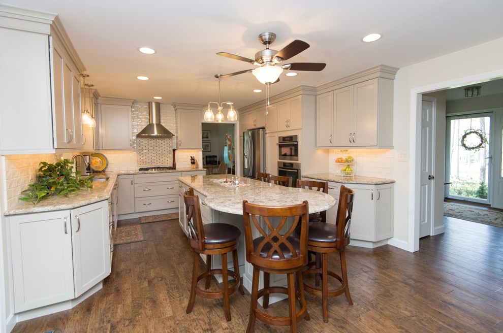 Example of a transitional u-shaped vinyl floor and brown floor eat-in kitchen design with an undermount sink, shaker cabinets, quartz countertops, subway tile backsplash, stainless steel appliances and an island