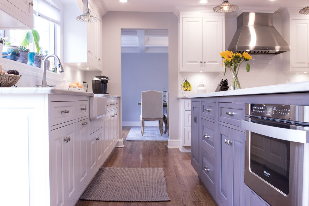 Photo of a l-shaped kitchen in New York with a farmhouse sink, beaded inset cabinets, white cabinets, granite benchtops, white splashback, subway tile splashback, stainless steel appliances, medium hardwood floors, with island and brown floor.
