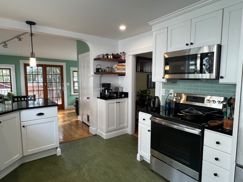 Mid-sized transitional l-shaped eat-in kitchen in Boston with a farmhouse sink, shaker cabinets, white cabinets, quartz benchtops, green splashback, ceramic splashback, stainless steel appliances, linoleum floors, a peninsula, green floor and black benchtop.