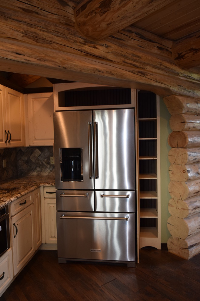 Example of a mountain style u-shaped dark wood floor eat-in kitchen design with a farmhouse sink, raised-panel cabinets, white cabinets, granite countertops, beige backsplash, stone tile backsplash, stainless steel appliances and an island