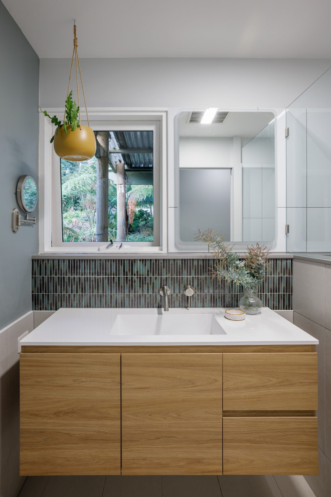 Пример оригинального дизайна: маленькая ванная комната в современном стиле с светлыми деревянными фасадами, душем в нише, унитазом-моноблоком, белой плиткой, плиткой мозаикой, зелеными стенами, полом из керамогранита, душевой кабиной, подвесной раковиной, столешницей из искусственного камня, серым полом, открытым душем, белой столешницей, подвесной тумбой и плоскими фасадами для на участке и в саду