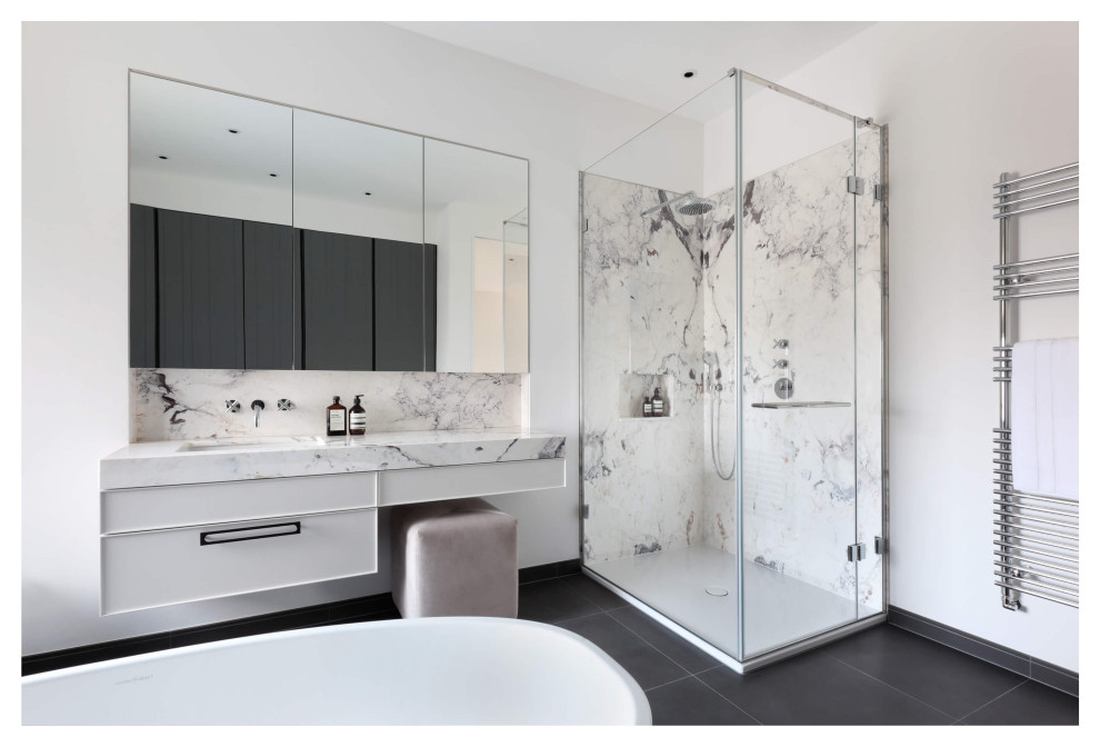 This is an example of a large contemporary master bathroom in London with raised-panel cabinets, white cabinets, a freestanding tub, a corner shower, white tile, marble, white walls, ceramic floors, an undermount sink, marble benchtops, grey floor, a hinged shower door, white benchtops, a single vanity, a built-in vanity and brick walls.