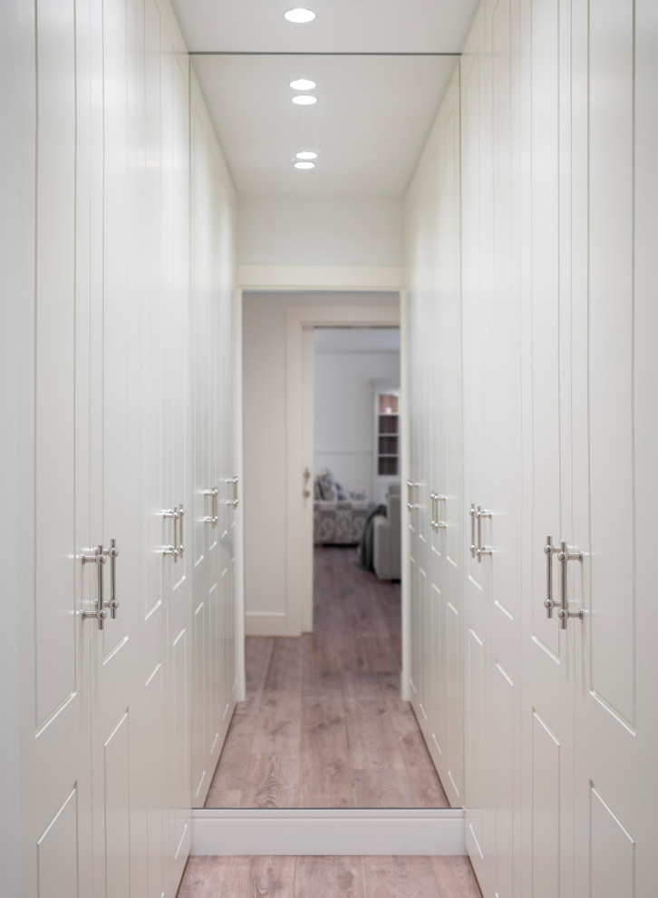 Photo of a mid-sized transitional gender-neutral dressing room in Bilbao with raised-panel cabinets, white cabinets, laminate floors and brown floor.