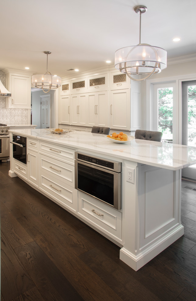 Photo of a large transitional u-shaped eat-in kitchen in Philadelphia with an undermount sink, recessed-panel cabinets, white cabinets, quartzite benchtops, white splashback, ceramic splashback, white appliances, dark hardwood floors, with island, brown floor and white benchtop.